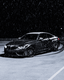 a black car is parked in a parking lot with snow falling