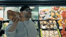 a man holding a large piece of bread in front of a display of fruits and vegetables with a price tag of 2.99