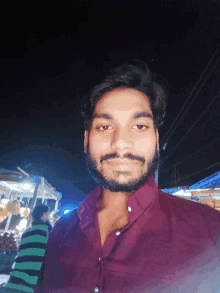 a man with a beard wearing a purple shirt smiles for the camera