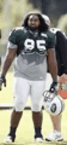 a football player in a green jersey and white shorts is standing on a field .