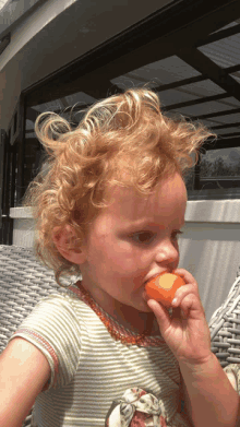 a little girl with curly red hair is eating an orange