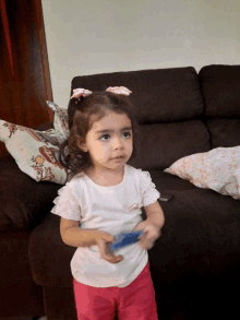 a little girl standing in front of a couch with a pillow on it