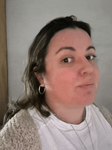 a woman wearing hoop earrings and a necklace looks at the camera