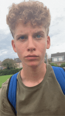 a young man with curly hair and blue eyes is wearing a green shirt and a blue backpack