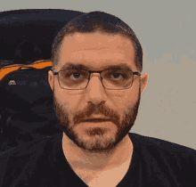 a man with a beard and glasses is wearing a black shirt and looking at the camera .