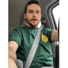 a man in a green shirt is sitting in a car with a seat belt on