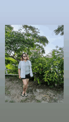 a woman wearing sunglasses and flip flops stands in front of trees