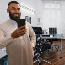 a man with a beard is taking a selfie in an office .