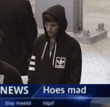 a man wearing an adidas hoodie is standing in front of a news report