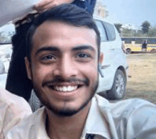 a man with a beard is smiling for the camera while taking a selfie in front of a car .