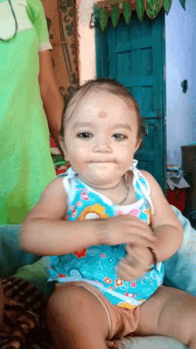 a baby wearing a blue tank top with flowers on it looks at the camera