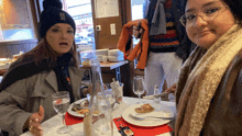 two women sit at a table with plates of food and glasses of water