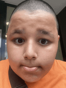 a young boy with a shaved head is making a face