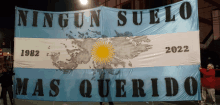 a man holds up a flag that says ' ningun suelo mas querido ' on it