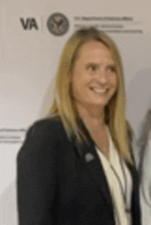 a woman in a black jacket and white shirt is smiling in front of a wall .