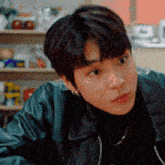 a young man wearing a black turtleneck and a leather jacket is sitting in a kitchen .