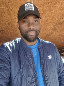 a man wearing a starter jacket and a hat