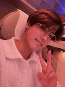 a young man wearing glasses and a white shirt is giving the peace sign