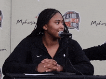 a woman is sitting at a table with a microphone in front of a wall that says basketball hall of fame