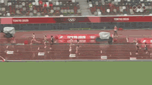 a group of people are running on a track in a stadium with the olympic rings on the wall .