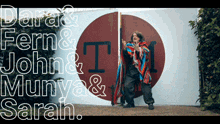 a woman in a colorful poncho is standing in front of a sign that says dara & fern & john & munya & sarah