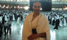 a man in a white robe is standing in front of a crowd in a mosque .