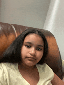 a girl with long hair is sitting on a brown leather chair