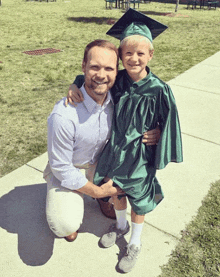 a man kneeling next to a young boy wearing a green cap and gown