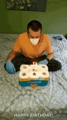 a man wearing a mask and gloves is sitting on a bed with a birthday cake made out of toilet paper rolls