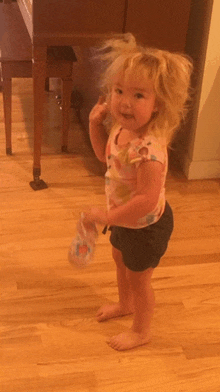 a little girl is standing on a wooden floor holding a bottle of water