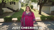 a woman in a pink dress is standing in front of a house with the words just checking in behind her