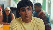 a young man in a yellow shirt is sitting at a table in a restaurant .