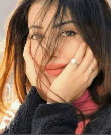 a close up of a woman covering her face with her hands and wearing a ring .