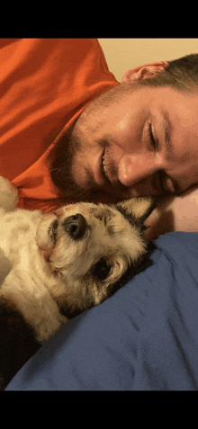 a man in an orange shirt is laying on a bed with his dog