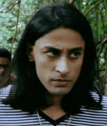 a man with long hair is wearing a black and white striped shirt and looking at the camera .