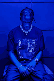 a man wearing a t-shirt that says ' travis scott ' on it is sitting in front of a blue wall