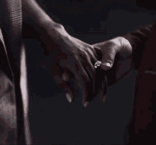 a close up of a person holding another person 's hand with a ring on their finger .