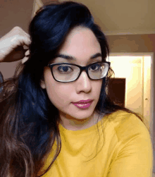 a woman wearing glasses and a yellow shirt is taking a selfie