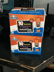 two boxes of elmer 's 30 washable disappearing purple school glue sticks on a table