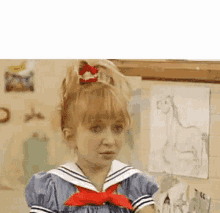 a girl in a sailor dress with a red bow in her hair is standing in front of a wall with drawings on it .