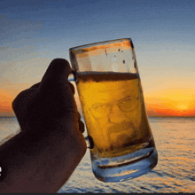 a person is holding a glass of beer with a picture of a man 's face on it