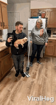 a man is holding a cat while a woman mops the floor in a kitchen with viralhog written on the bottom