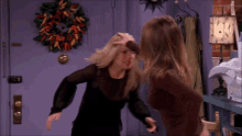 two women fighting in front of a purple door with a wreath on it