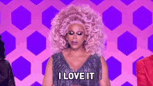 a drag queen with a big pink wig is saying i love it