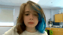 a girl with blue hair looks at the camera in a kitchen