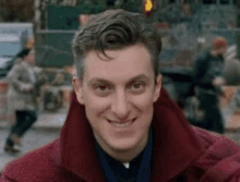 a close up of a man wearing a red coat and smiling on a city street .