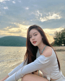 a woman in a white top sits on a beach