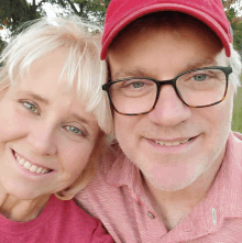 a man wearing glasses and a red hat is smiling next to a woman