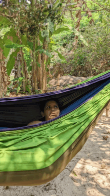 a woman is laying in a green hammock on a beach