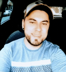 a man wearing a hat and a blue shirt is taking a selfie in the back seat of a car .